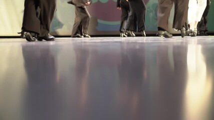 Women's feet in black shoes. In stage costumes, they tap dance on a hard floor illuminated by light. A light kick. Selective focus. High quality 4k footage