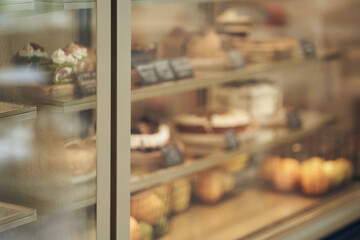 Unfocused sweet pastries. A showcase in a pastry shop. A glass counter with cakes, pastries and tartlets. Refrigerator shelves with sweets. With space to copy. High quality photo