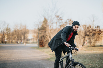 Young man in casual attire enjoys a bike ride in an urban park at sunset, exuding a sense of freedom and relaxation.