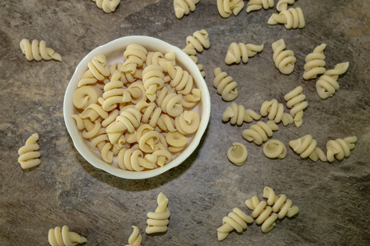 Top view of dry trottole pasta in a bowl and scattered noodles around with selective focus.
