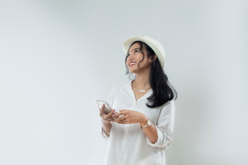 Beautiful young Asian woman tourist in straw hat standing posing with hand holding her smart phone and while looking at the copy space above her, woman advertising online purchase