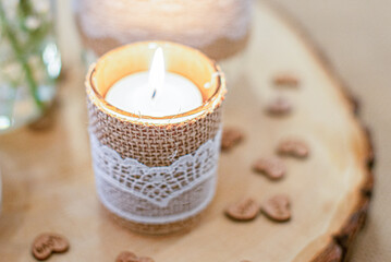 Warm lit candle wrapped in brown canvas and white lace on tree bark and miniature hearts in background