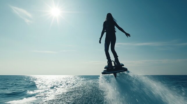 Silhouette of a person enjoying a flyboarding session over the ocean against a bright sunlit sky.
