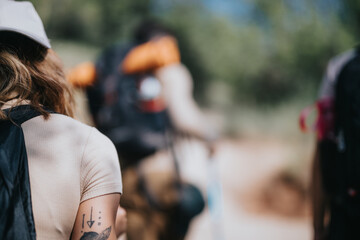 Close-up of a woman's tattooed arm as a group of friends hike on a sunny day, showcasing outdoor adventure and friendship.