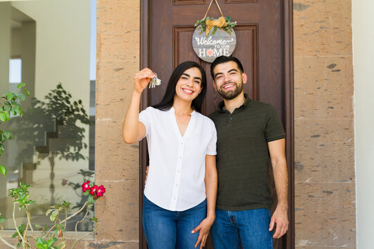 Newlywed couple happily posing in front of their new home with keys and a welcome sign