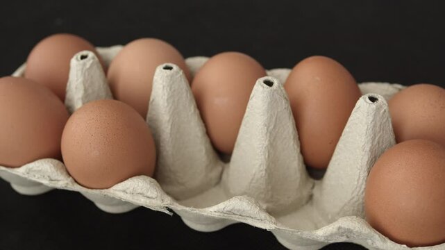 Close up of male hand taking many organic farm eggs. Picking white eggs from an egg carton on dark background. 