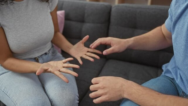 A man and woman communicate with hand gestures while sitting on a couch, symbolizing a conversation or discussion in a home setting.