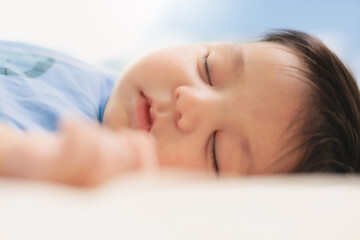 Newborn baby boy sleeping in a blue bodysuit on the bed