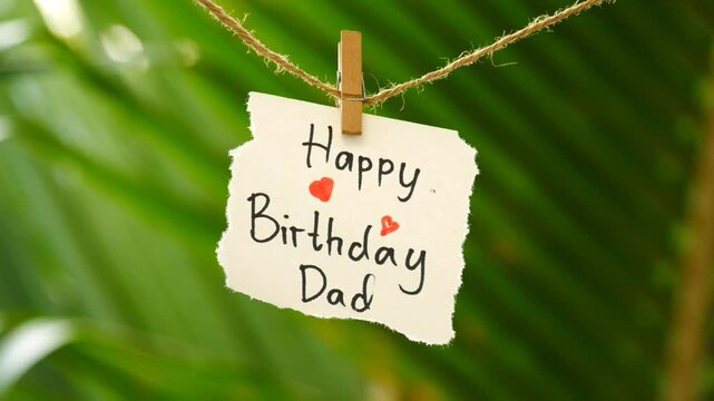 Happy birthday dad - Torn note paper with the text Happy birthday daddy hanging and swinging on a rope, nature bokeh sunset in the background