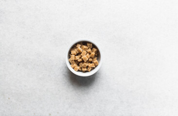 Overhead view of peanut butter fudge pieces in a white ceramic ramekin, top view of soft peanut fudge squares on a white background