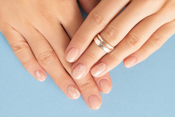 Beautiful womans hands with nude nail design on blue background. Manicure, pedicure beauty salon concept