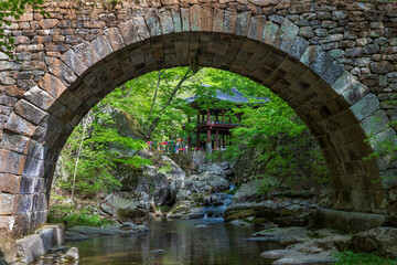 Seungju-eup, Suncheon-si, Jeollanam-do, South Korea - April 22, 2023: Spring view of Seungseongyo Bridge on water and rock of valley against pavilion at Seonamsa Temple
