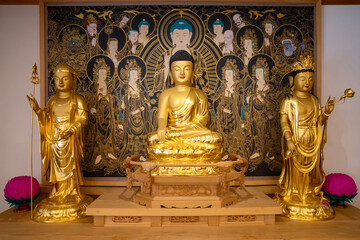 Seongbuk-dong, Seongbuk-gu, Seoul, South Korea - May 26, 2023: Front view of three golden yellow Buddha statue and altar paintings in Buddhist sanctuary of Gilsangsa Temple
