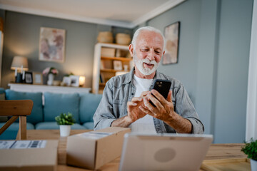 senior man sit at home hold post package delivery use mobile phone