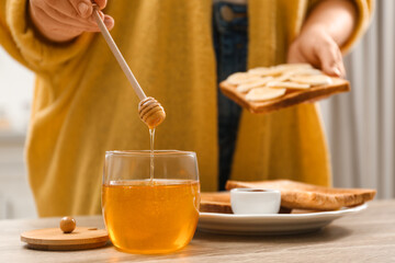 Woman pouring honey onto toast with banana at table indoors, closeup