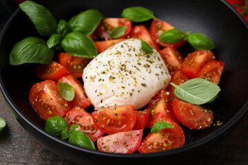 Tasty salad Caprese with mozarella, tomatoes and basil in black bowl, closeup