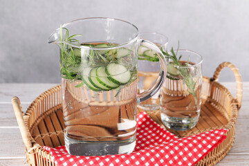 Refreshing cucumber water with rosemary in jug and glass on light wooden table