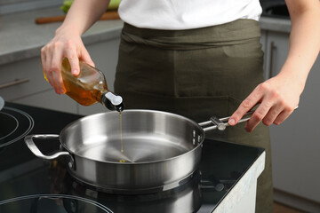 Vegetable fats. Woman pouring oil into frying pan on cooktop in kitchen, closeup