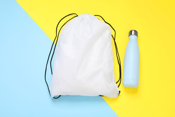 White drawstring bag and thermo bottle on color background, flat lay