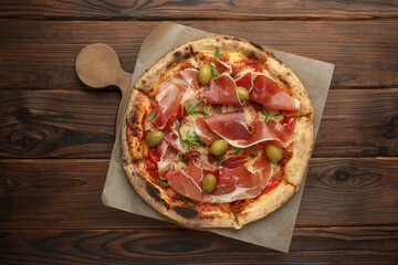 Tasty pizza with cured ham, olives and sun-dried tomato on wooden table, top view