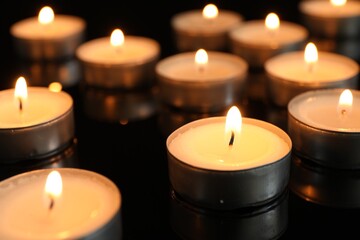 Many burning tealight candles on black background, closeup