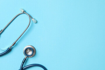 Stethoscope on light blue background, top view. Space for text