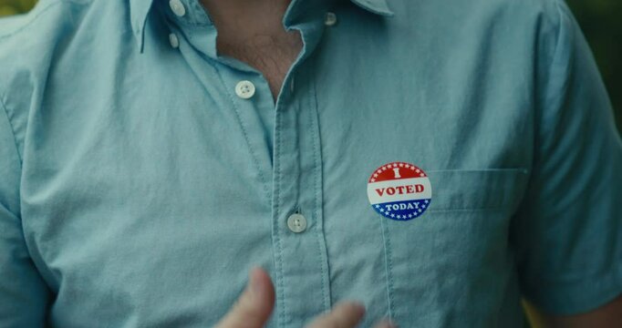 Young man smiling with an &lsquo;I Voted&rsquo; sticker and pin 