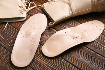 Boots and leather orthopedic insoles on wooden background