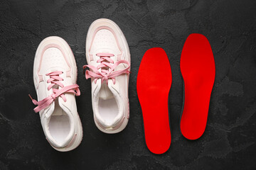 Sneakers and red orthopedic insoles on black grunge background