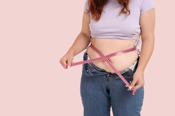 Overweight woman in tight jeans measuring her belly on pink background. Excess weight concept
