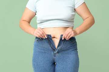 Overweight woman in tight jeans on green background. Excess weight concept