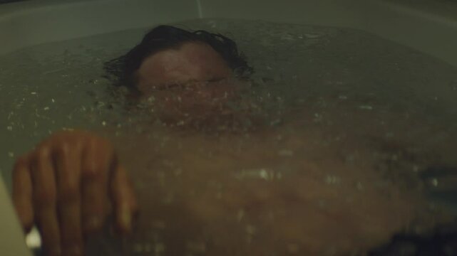 Athlete in bath tub full of ice lying and submerging his head