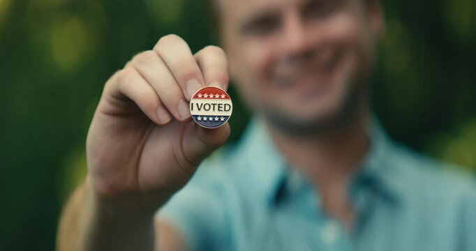 Young man smiling with an &lsquo;I Voted&rsquo; sticker and pin 
