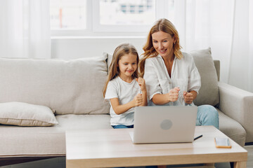 Mother and daughter sharing quality time on couch while using laptop for learning and entertainment