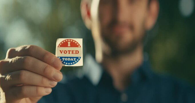 Young man smiling with an &lsquo;I Voted&rsquo; sticker and pin 