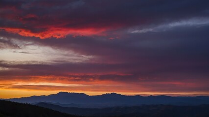 Fototapeta premium Sky turning red and purple as the sun sets behind the mountains, creating a serene twilight scene