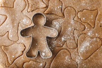 Cooking ginger cookies, Christmas and New Year traditional cookies in shape of gingerbread man, raw rolled out dough with cut out dough figures, closeup texture, top view, metal pastry cutter on dough
