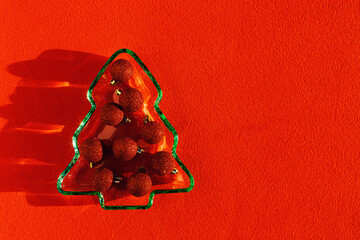 Plate as New Year tree with shining red Christmas balls on red textile, Christmas tree from green glowing glass glare. Sunlight and shadow, sparkling holiday food, xmas trendy still life