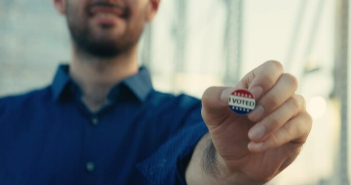 Young man smiling with an &lsquo;I Voted&rsquo; sticker and pin 