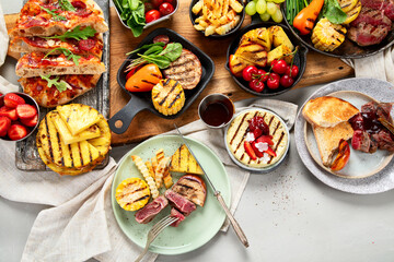Table with grilled food. Pizza, corn, tomatoes, peppers, cooked meat. BBQ time