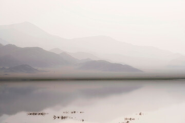 morning mountain landscape, peaks and hills in a foggy haze are reflected in the calm water of the lake