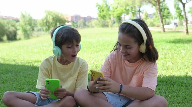 Boy And Girl Having Fun Together Outdoors Playing Video Games Or Watching Videos On The Internet Using Mobile Phone And Headphones.