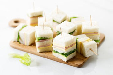 Sandwich of white soft bread with ham, cheese and lettuce on wooden board.