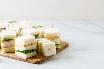Sandwich of white soft bread with ham, cheese and lettuce on wooden board.
