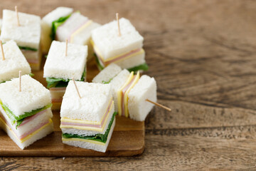 Sandwich of white soft bread with ham, cheese and lettuce on wooden board.