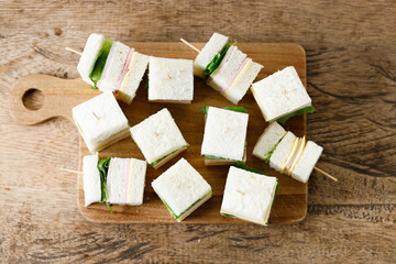 Sandwich of white soft bread with ham, cheese and lettuce on wooden board.