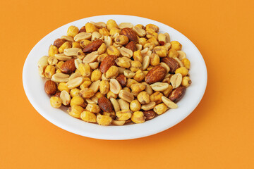 Roasted peanuts, corn and almonds in a plate on an orange background
