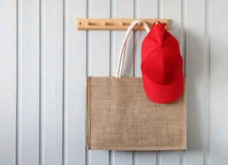 summer bag and a red baseball cap hang on a wooden hanger on a white board wall in the cottage....