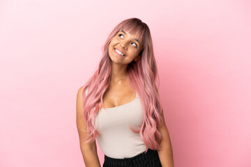 Young mixed race woman with pink hair isolated on pink background thinking an idea while looking up