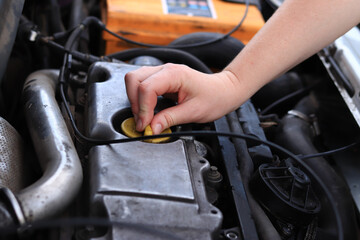 Fototapeta premium Change of oil. A woman's hand opens or closes the oil filler cap. Changing the oil in a diesel car engine. Car maintenance. Old car